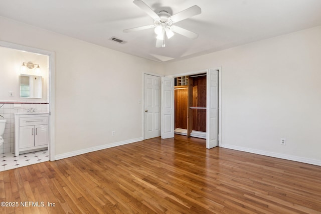 unfurnished bedroom featuring sink, hardwood / wood-style flooring, ensuite bathroom, and ceiling fan