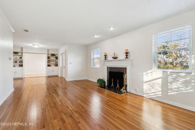 unfurnished living room with crown molding, wood-type flooring, built in features, and a fireplace