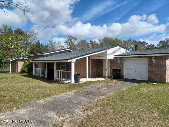 view of front of home with a porch, an attached garage, brick siding, driveway, and a front yard