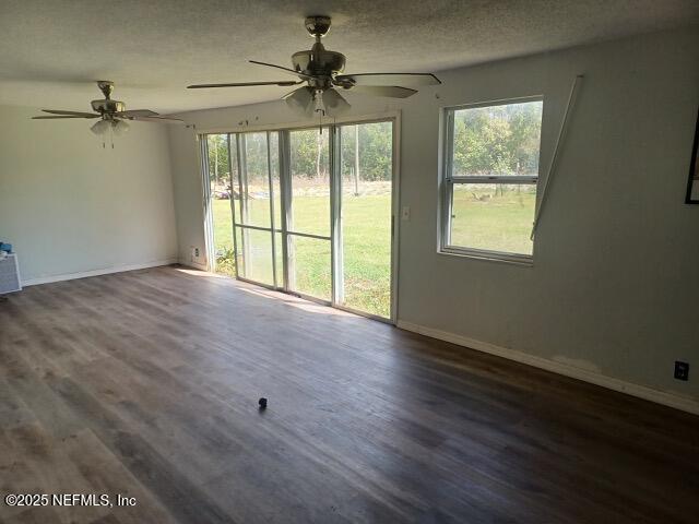 unfurnished living room with a ceiling fan, baseboards, dark wood finished floors, and a textured ceiling