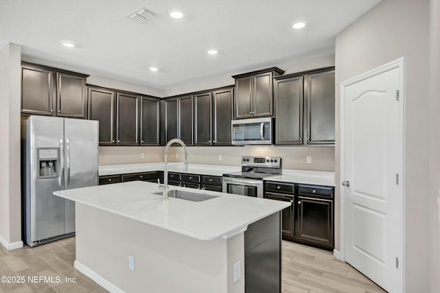 kitchen with dark brown cabinets, stainless steel appliances, sink, and a center island with sink