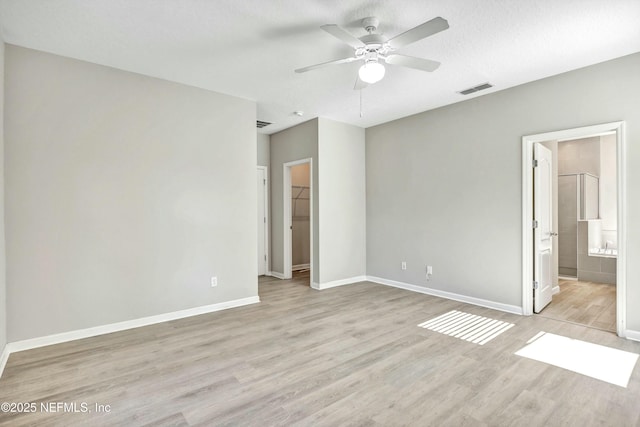 unfurnished bedroom with ensuite bathroom, light wood-type flooring, a spacious closet, a textured ceiling, and a closet