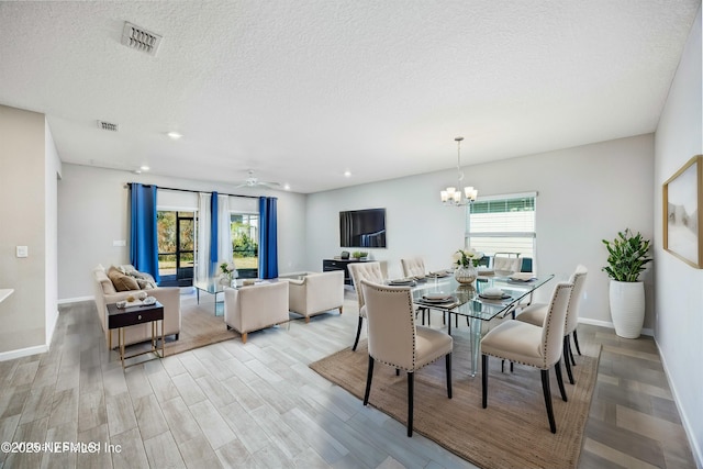 dining space with ceiling fan with notable chandelier, a wealth of natural light, light hardwood / wood-style floors, and a textured ceiling