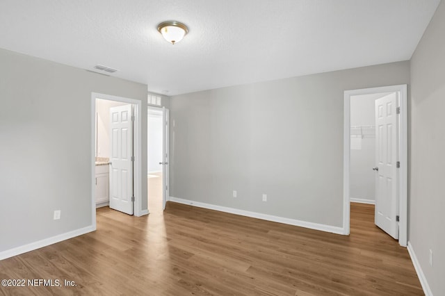 unfurnished bedroom featuring ensuite bath, hardwood / wood-style flooring, a spacious closet, and a closet