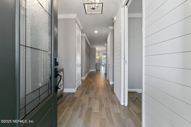 corridor with a textured ceiling, light hardwood / wood-style floors, ornamental molding, and a notable chandelier