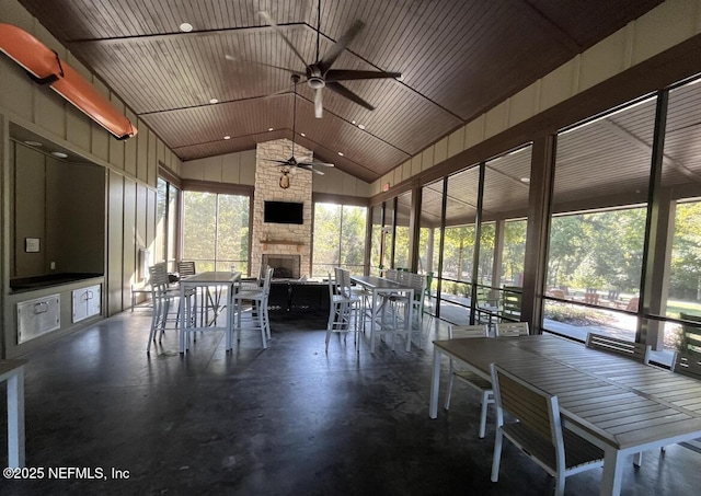 unfurnished sunroom featuring a stone fireplace, ceiling fan, and vaulted ceiling