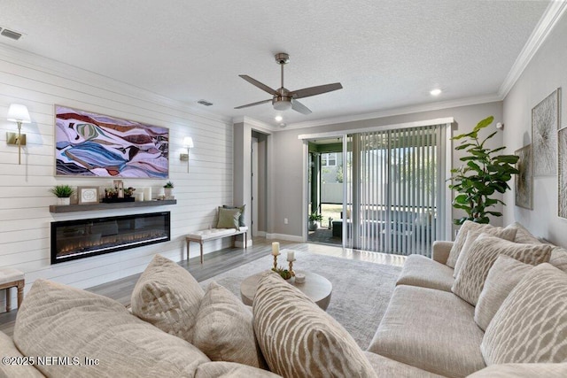 living room featuring a large fireplace, crown molding, hardwood / wood-style floors, a textured ceiling, and wooden walls