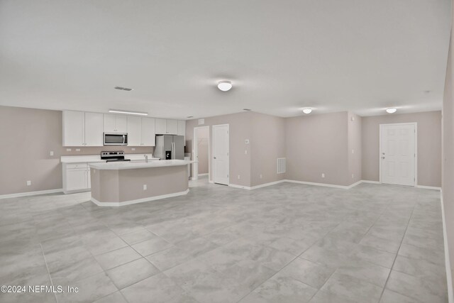 kitchen with white cabinets, stainless steel appliances, a kitchen island with sink, and light tile patterned flooring