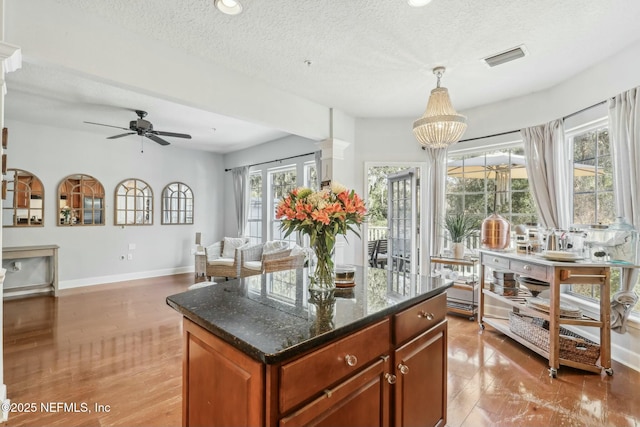 kitchen featuring decorative light fixtures, dark stone countertops, a center island, a textured ceiling, and ceiling fan with notable chandelier