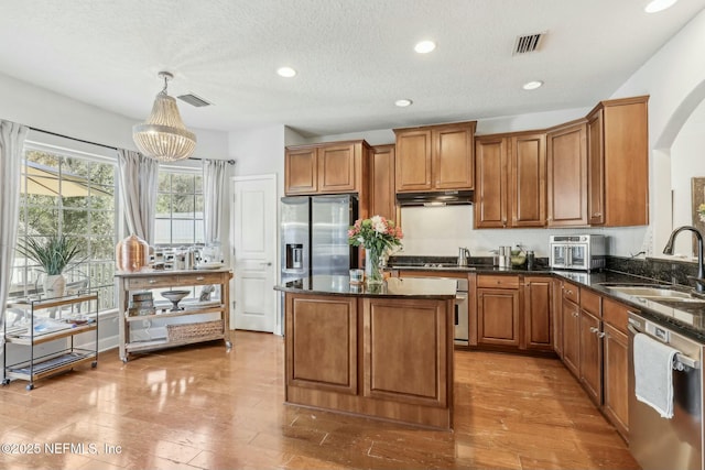 kitchen with sink, hanging light fixtures, stainless steel appliances, a textured ceiling, and dark stone counters