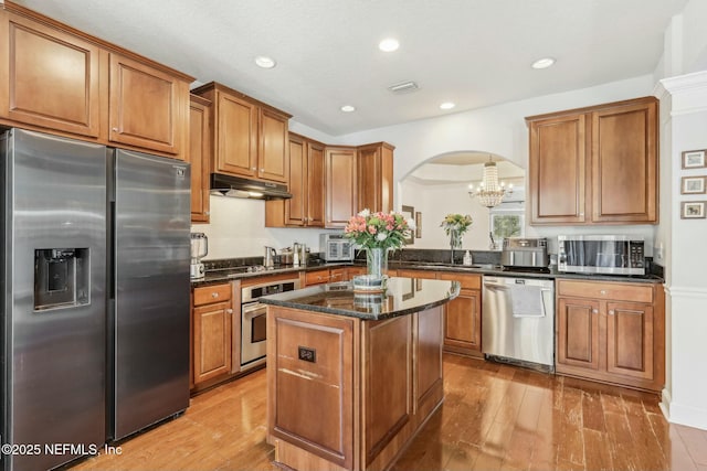 kitchen featuring appliances with stainless steel finishes, light hardwood / wood-style floors, a kitchen island, and decorative light fixtures