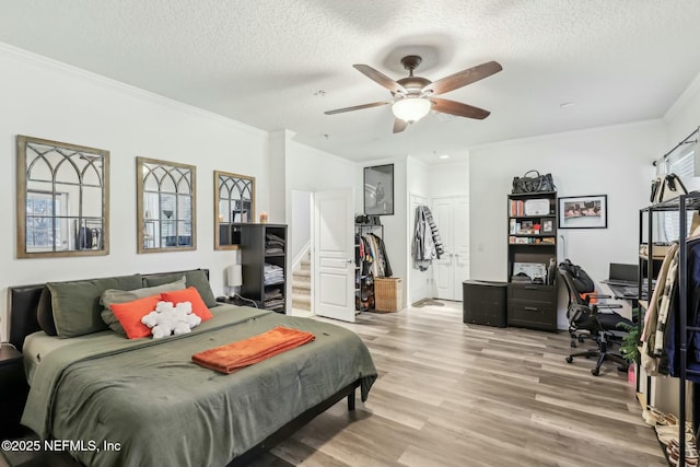 bedroom with ceiling fan, light hardwood / wood-style floors, crown molding, a textured ceiling, and a closet