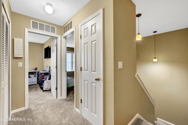 hallway featuring light colored carpet and a textured ceiling