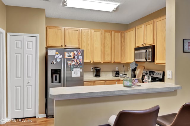 kitchen with appliances with stainless steel finishes, a kitchen bar, light brown cabinets, kitchen peninsula, and light hardwood / wood-style flooring