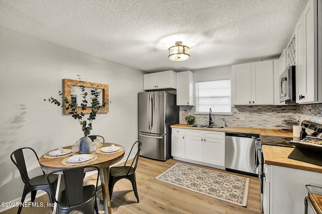 kitchen with sink, stainless steel appliances, wood counters, tasteful backsplash, and white cabinets