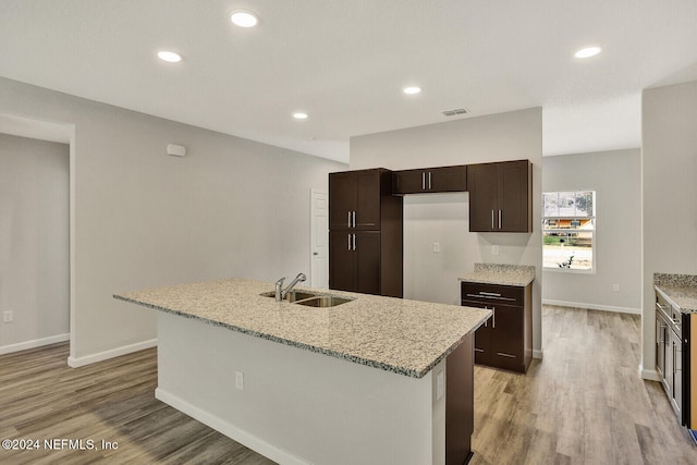 kitchen featuring a kitchen island with sink, sink, light stone countertops, and light hardwood / wood-style flooring