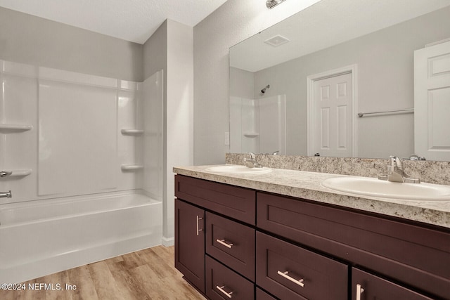 bathroom with hardwood / wood-style floors, vanity,  shower combination, and a textured ceiling