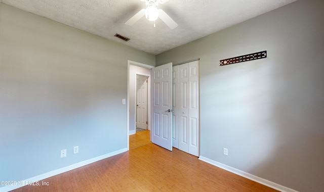 unfurnished bedroom with ceiling fan, a closet, light hardwood / wood-style floors, and a textured ceiling