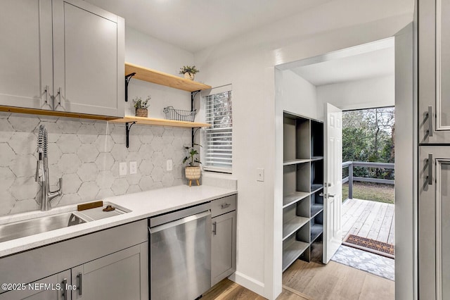 kitchen featuring gray cabinetry, sink, stainless steel dishwasher, light wood-type flooring, and tasteful backsplash