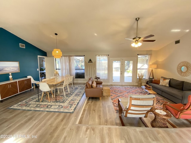 living room with ceiling fan, french doors, light hardwood / wood-style floors, and vaulted ceiling