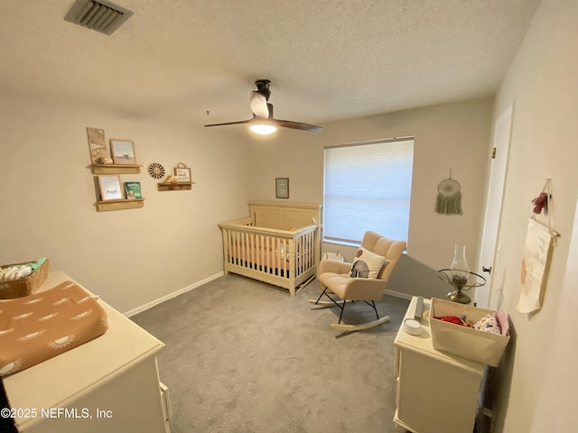 carpeted bedroom featuring a textured ceiling, ceiling fan, and a crib