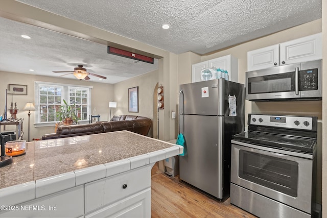 kitchen with white cabinetry, ceiling fan, stainless steel appliances, light hardwood / wood-style floors, and a textured ceiling