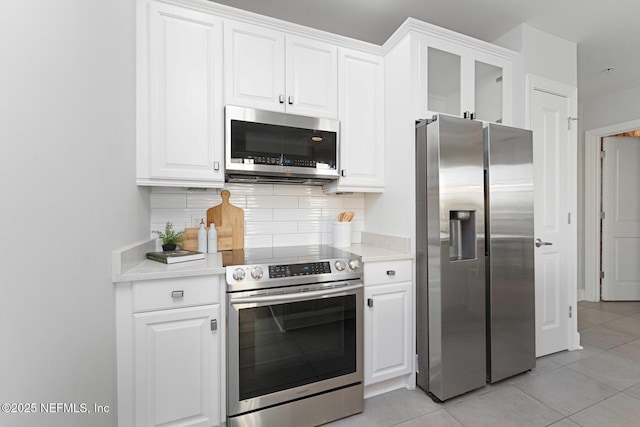 kitchen featuring decorative backsplash, appliances with stainless steel finishes, white cabinetry, and light tile patterned flooring