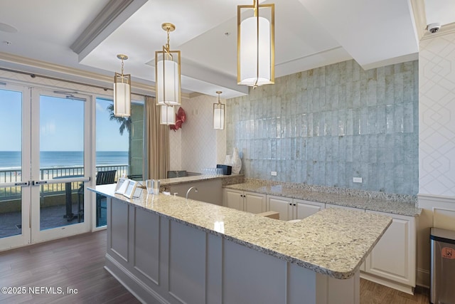 kitchen featuring pendant lighting, a water view, light stone counters, dark hardwood / wood-style flooring, and white cabinetry