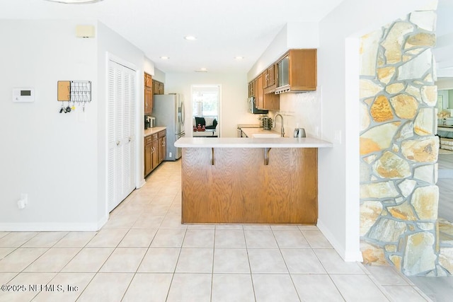 kitchen with stainless steel refrigerator, sink, kitchen peninsula, a breakfast bar area, and light tile patterned flooring