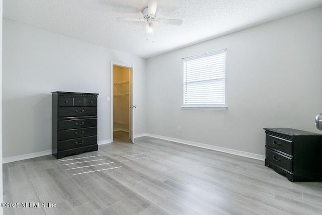 unfurnished bedroom with a textured ceiling, ceiling fan, a spacious closet, light hardwood / wood-style floors, and a closet