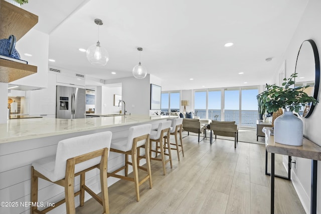 kitchen with a water view, stainless steel fridge, light stone countertops, decorative light fixtures, and a wall of windows