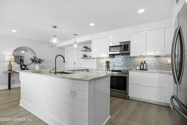 kitchen with white cabinetry, sink, tasteful backsplash, a center island with sink, and appliances with stainless steel finishes