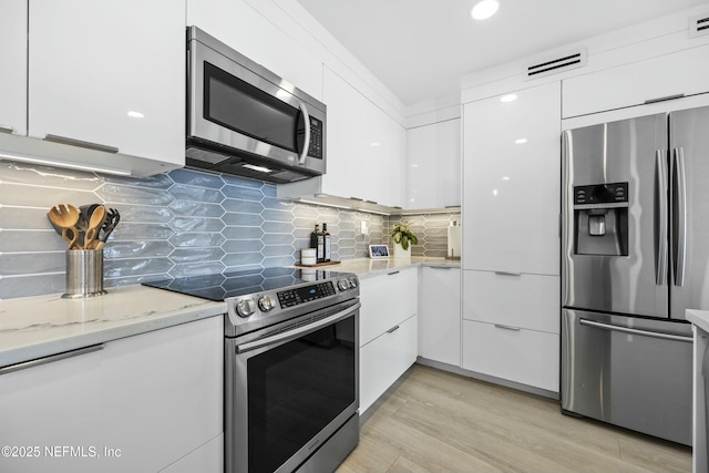 kitchen featuring white cabinets, light stone countertops, stainless steel appliances, and tasteful backsplash