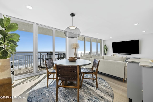 dining space featuring a water view, light hardwood / wood-style flooring, and a wall of windows