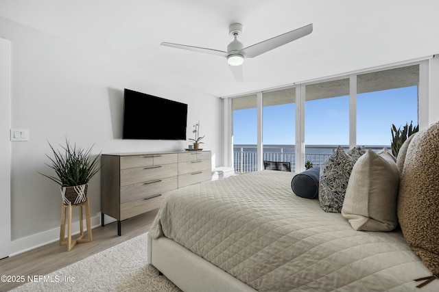 bedroom featuring access to outside, ceiling fan, expansive windows, and light wood-type flooring