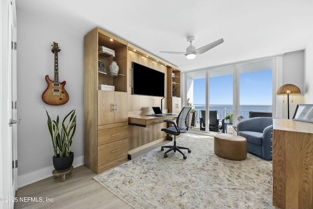 home office with light wood-type flooring, floor to ceiling windows, and ceiling fan