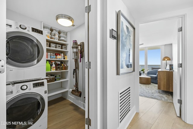 laundry area with light wood-type flooring and stacked washer and clothes dryer