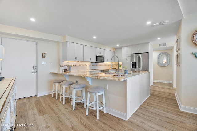 kitchen featuring white cabinetry, backsplash, stainless steel appliances, light hardwood / wood-style floors, and kitchen peninsula