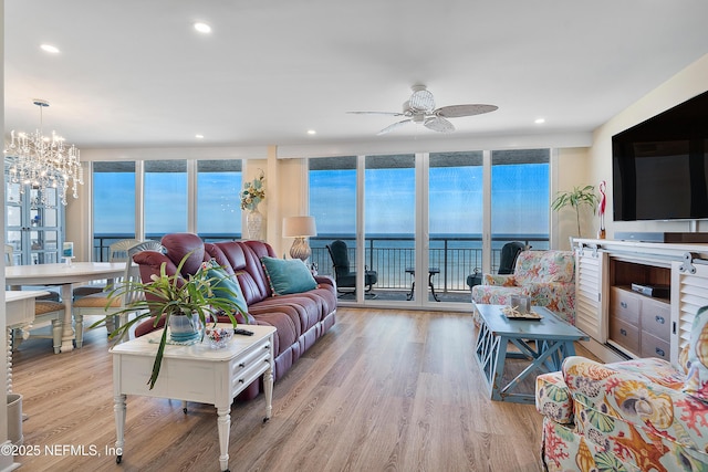 living room with ceiling fan with notable chandelier, light hardwood / wood-style floors, and expansive windows