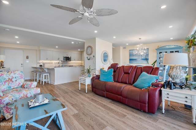 living room featuring sink, ceiling fan with notable chandelier, and light hardwood / wood-style floors