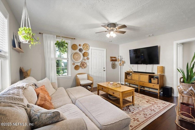 living room featuring ceiling fan, dark wood-type flooring, and a textured ceiling