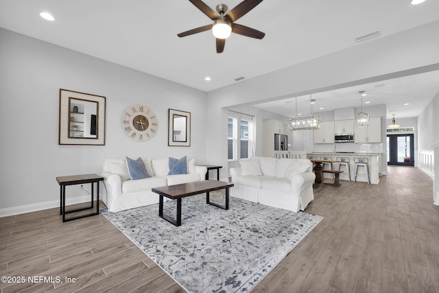 living room with ceiling fan with notable chandelier and light wood-type flooring