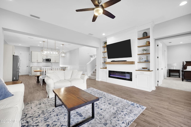 living room with light hardwood / wood-style floors, ceiling fan, a large fireplace, and built in features