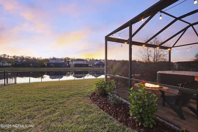 yard at dusk with glass enclosure, a water view, and a hot tub