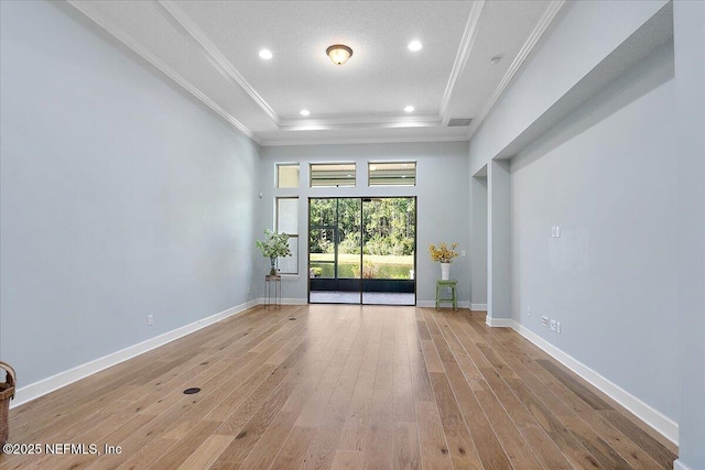 empty room with a textured ceiling, light wood-type flooring, a raised ceiling, and ornamental molding