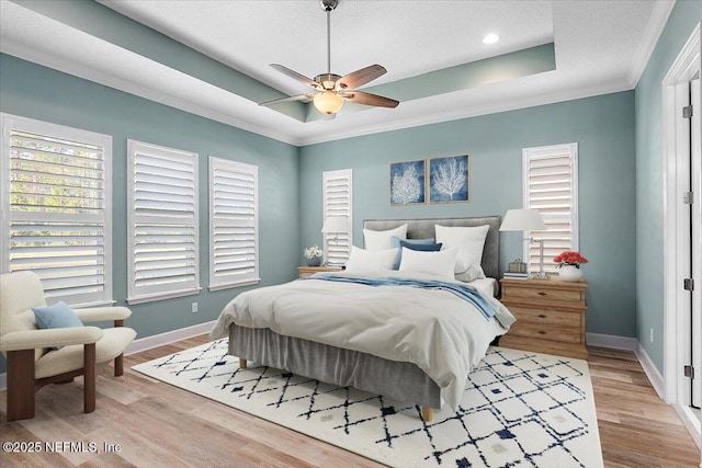 bedroom with light wood-type flooring, ornamental molding, a textured ceiling, a tray ceiling, and ceiling fan