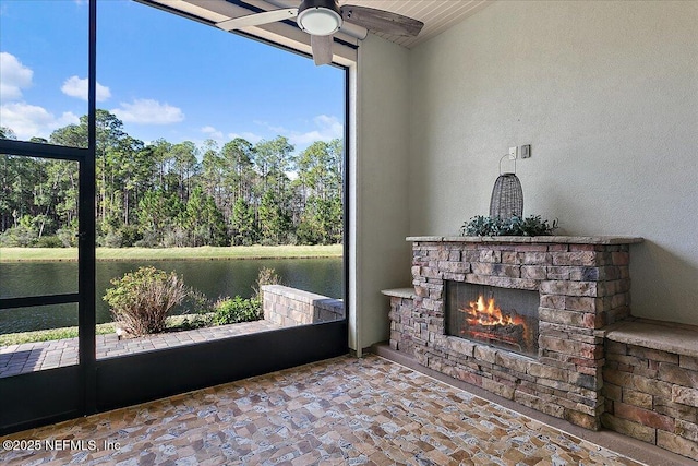 sunroom / solarium featuring an outdoor stone fireplace, ceiling fan, and a water view