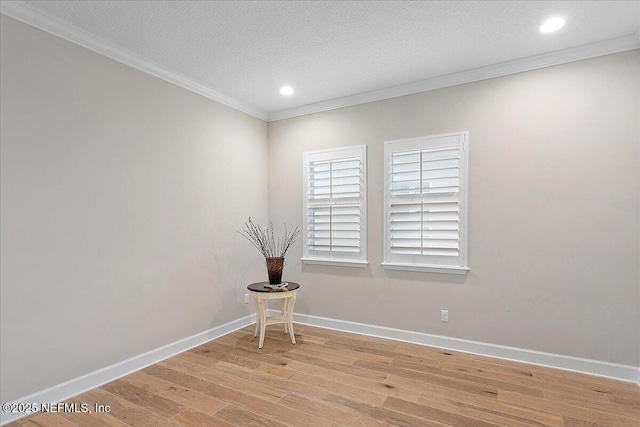 empty room featuring a textured ceiling, light hardwood / wood-style flooring, and crown molding