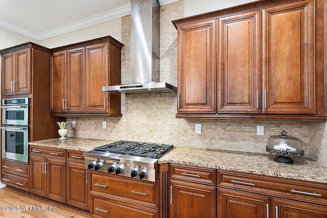 kitchen featuring appliances with stainless steel finishes, tasteful backsplash, light stone counters, wall chimney exhaust hood, and crown molding