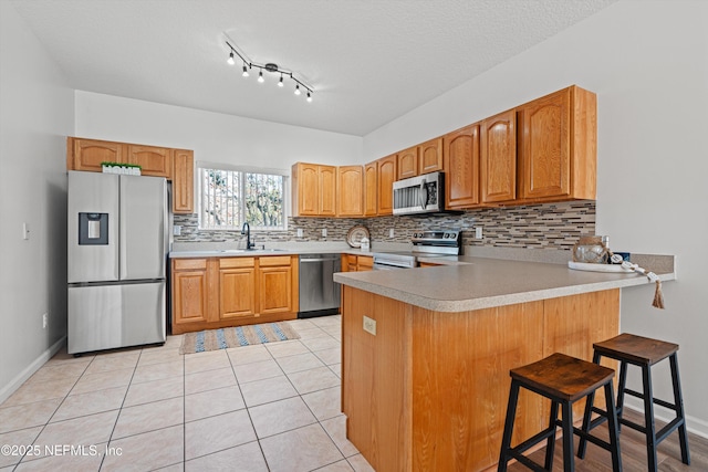 kitchen with sink, decorative backsplash, appliances with stainless steel finishes, light tile patterned flooring, and a breakfast bar area